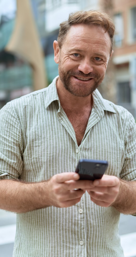 Ein lächelnder Mann schaut dich an und hält sein Handy mitten in einer Stadt.