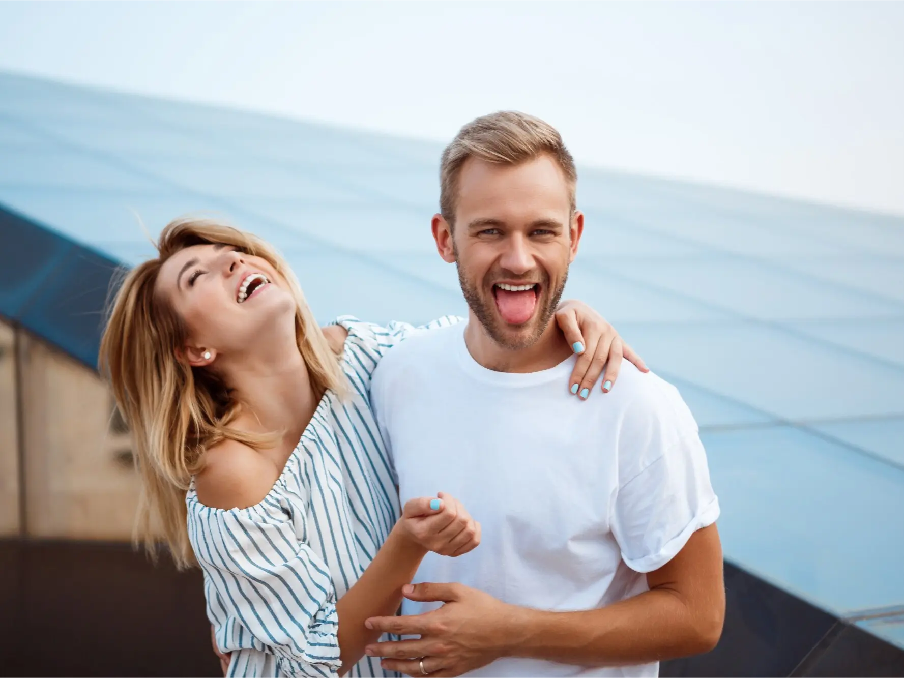 Glückliches junges Paar lacht ausgelassen im Freien – Frau in gestreiftem Sommerkleid und Mann im weißen T-Shirt genießen unbeschwerte Momente – Symbol für Lebensfreude und echte Verbindung